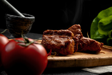 spicy ribs served on a board with hot chili peppers, on a dark background