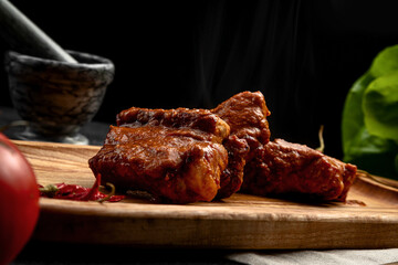spicy ribs served on a board with hot chili peppers, on a dark background