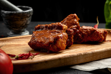 fried ribs in sauce served on a board, on a dark background