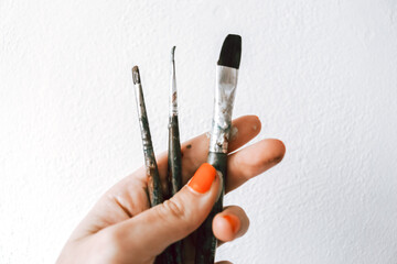 Paint brushes held in hand with painted orange finger nail polish artist studio on blank white background