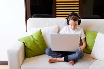 Concentrated schoolboy wearing headphones with laptop play online games at home. Distance learning in quarantine