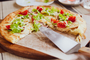 Fresh pizza with tomatoes, cheese and bacon on a wooden board with a scapula close-up.