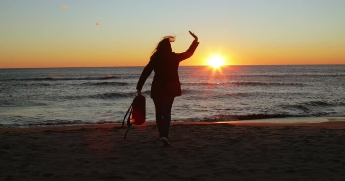 silhouette of girl has fun by the ocean at sunrise on the beach in winter