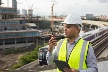 Asian engineer handsome man or architect use radio communication with white safety helmet in city...