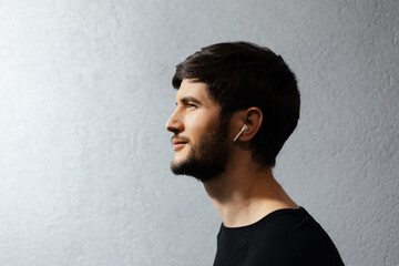Side portrait of smiling young man using earbuds on textured background.