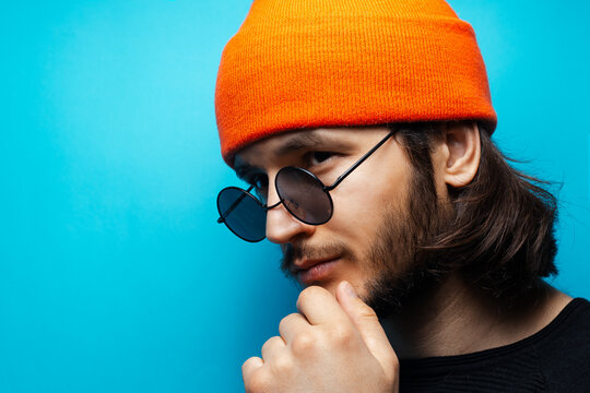 Young man with long hair on blue background. Wearing sunglasses and hat.