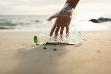 Close up woman hand pick up the plastic bottle on the beach. Female Volunteer clean the trash on the beach make the sea beautiful. World environment day concept.