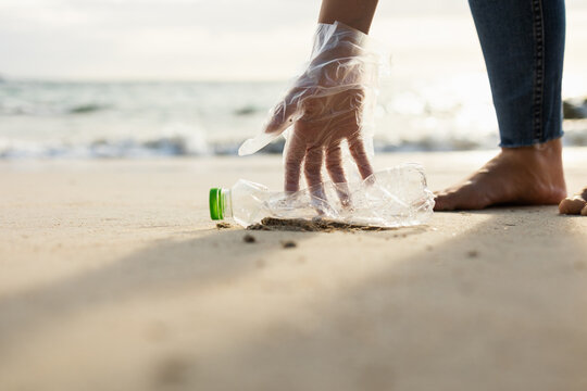 Close Up Woman Hand Pick Up The Plastic Bottle On The Beach. Female Volunteer Clean The Trash On The Beach Make The Sea Beautiful. World Environment Day Concept.