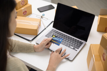 Fototapeta na wymiar Shopping online. Young asian woman input the serial number of credit card to laptop for shopping payment. Buy item online delivery at home. Small business entrepreneur with many parcel box on table