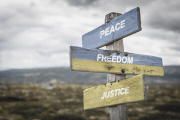 peace freedom justice text quote on wooden signpost outdoors, written on the ukranian flag.