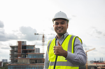 Asian engineer man or architect looking forward with white safety helmet in city construction site . Standing on rooftop building construction at capital.