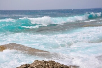 Perfect rolling wave crash into Croatian beach at island Losinj.  A big wave overlaps the coast of the Croatian island of Losinj. Rolling wave crashing on rocky coast.
