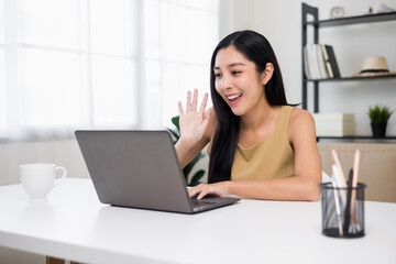 Young asian beautiful business woman working with laptop sitting at home. Smiling charming happy young female doing homework meeting conference with team at home.