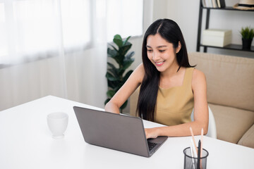 Young asian beautiful business woman working with laptop sitting at home. Smiling charming happy young female doing homework meeting conference with team at home.