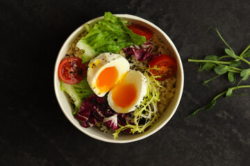 Healthy bowl with poached egg, bulgur, tomatoes and lettuce. on a dark background in an eco paper box. Healthy food delivery concept.