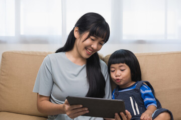 Obraz premium Happy asian family mother and son using tablet for education. Little boy watching funny social media. Mom with kid using tablet video call to father.