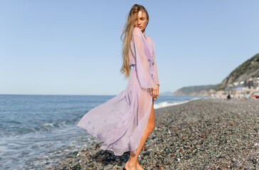 Young beautiful model in a light cape on the beach