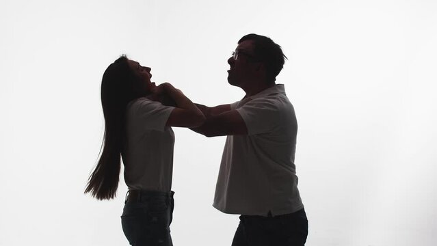 Silhouette of man from rage and anger strangling woman, white background in studio, side view. Man in fit of rage begins to strangle woman. Concept rage and madness