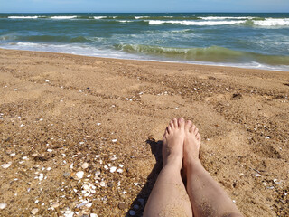 vista subjetiva de   pies sobre la arena de una playa con el mar de fondo
