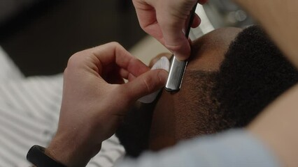 The barber shaves the contour of the temple of a man with a dangerous razor