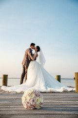 Fototapeta na wymiar Wedding bridal bouquet lies on the pier Wedding couple on the background Bride and groom kissing on the Pier 
