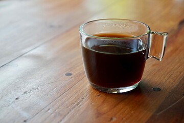 hot black coffee in transparent cup placed on wooden table in morning light.