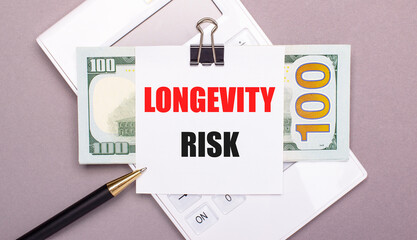 On a gray background, a white calculator, a pen, banknotes and a sheet of paper with the text LONGEVITY RISK.