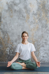 Happy girl in a tracksuit, sits on the floor in the lotus pose. A lady meditates,crossed fingers in Yoga Mudra. Assanas for Meditation and Relax