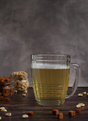 light beer in a glass mug with crackers and peanuts on a dark background