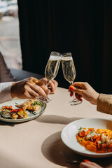 Closeup of a man and woman clinking glasses with champagne at a restaurant.