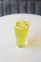 green lemonade with lemon in a glass glass on a white table with a blurred gray background.