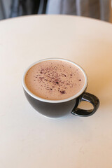 cocoa with lovanda in a black ceramic cup on a white table against a blurred gray background.