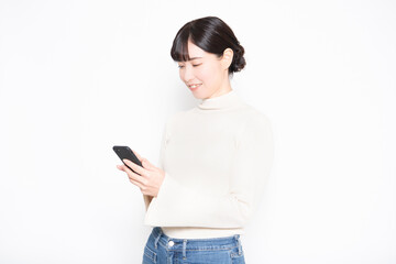 Fototapeta premium 白い背景の前に立って、スマホを操作する女性