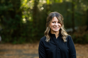 A young cosmetologist standing outside among green trees for a headshot with copy space