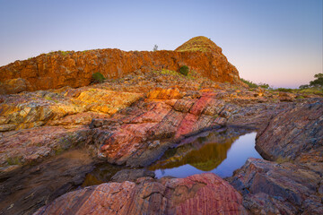 Fototapeta na wymiar Colorful landscape at dawn with rocks consisting of red layers of Jasper and little pond in the vicinity of the village of Marble Bar, Western Australia
