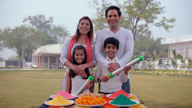 A modern Indian family wishes their friends / relatives on the occasion of Holi - an Indian festival  a happy family  a spring festival. Cute siblings standing together with their parents while hol...