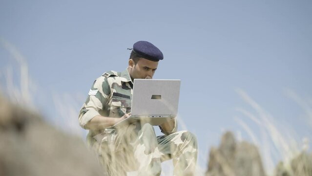 low angle shot of serviceman using laptop on top of mountain for gathering data - concept of intelligence, internet connection, communication and surveillance