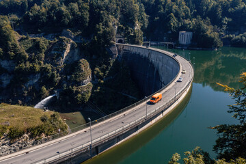 Fototapeta premium Aerial view of the Barrage de Rossens, a dam in the canton of Fribourg, Switzerland. Six vehicles are passing on the road that runs along the dam. Photograph taken in early fall.