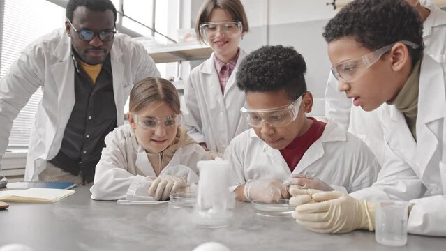Waist up slowmo of group of diverse students and their African American male teacher looking at lab smoke in flask while conducting chemical experiments at class during Science lesson