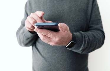midsection of man holding smartphone in hand in front of white wall