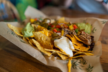 Plato de nachos con muchos condimentos en una mesa de madera y un refresco junto a la comida