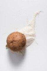 Coco abierto con carne de coco rallado que se derrama sobre una mesa blanca. Vista superior	