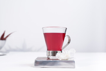 Una taza transparente de té de bayas sobre una mesa blanca y un fondo gris claro