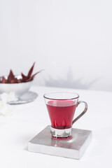 Una taza transparente de té de bayas sobre una mesa blanca y un fondo gris claro