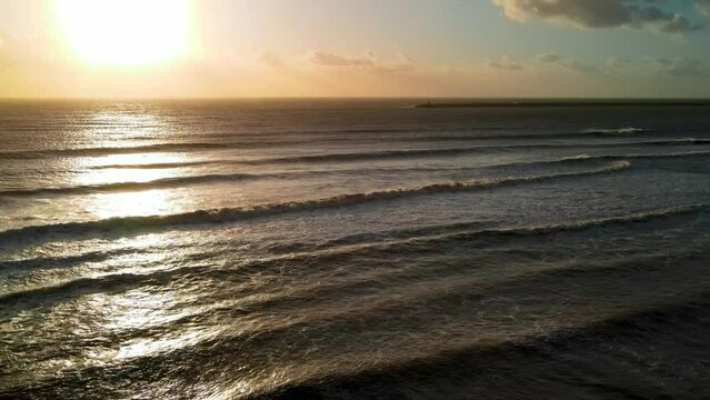 Sunset over the ocean from drone, aerial view of waves along the coastline, backlit view