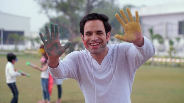 An excited young man in casual clothes showing his colorful hands during Holi celebrations - vibrant Gulal  a spring festival  enjoyment. A pretty female wearing trendy sunglasses enjoys playing th...