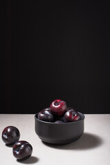 Ciruelas negras maduras en un plato negro sobre fondo negro	
