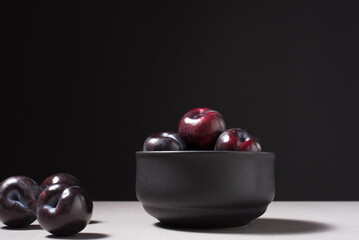Ciruelas negras maduras en un plato negro sobre fondo negro	
