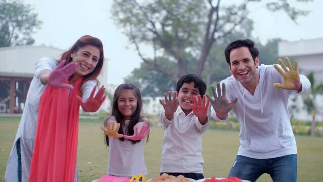 An excited Indian family showing their colorful hands together on the Holi festival - togetherness and bonding  an urban family. Cheerful siblings posing together for the camera with their parents ...