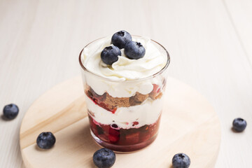 Trifle - traditional English dessert in glass on a light wooden table. Close up view.